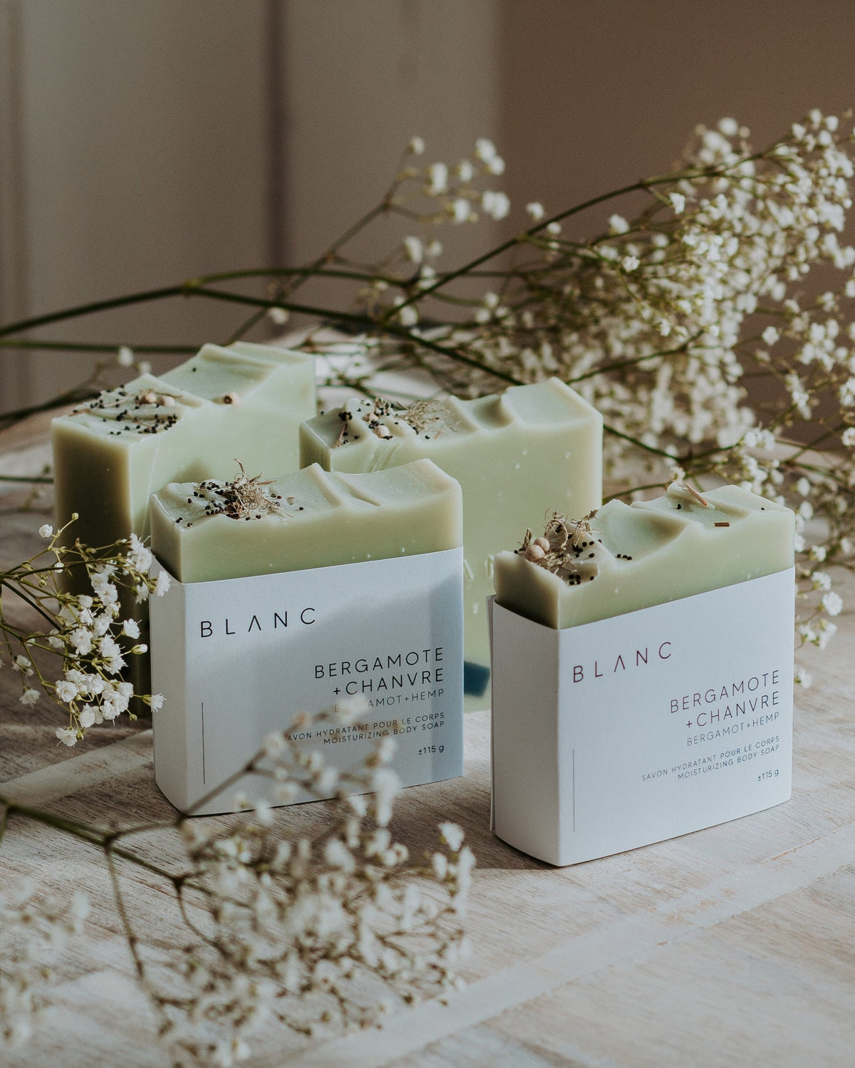 Des savons bergamote + chanvre disposés sur une table avec des fleurs de l'entreprise Blanc Savonnerie.
